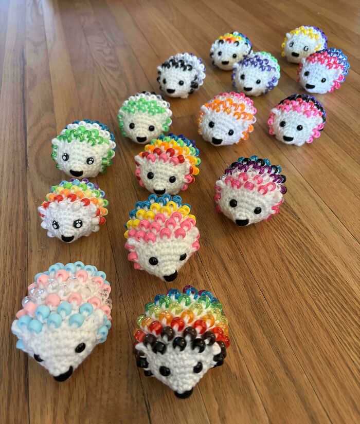 Colorful crocheted hedgehogs with beads arranged on a wooden floor, showcasing impressive crochet craftsmanship.