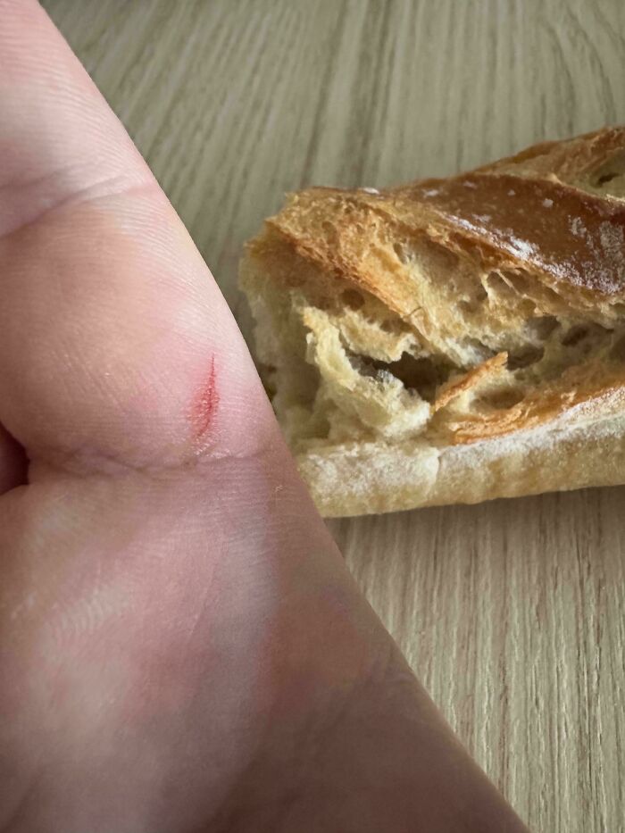 A hand with a small cut and a piece of bread on a wooden table; everyday life moments.
