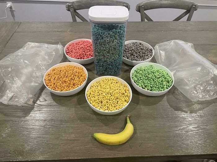 Bowls of colorful cereal rings and a banana on a table, presenting nothing interesting.