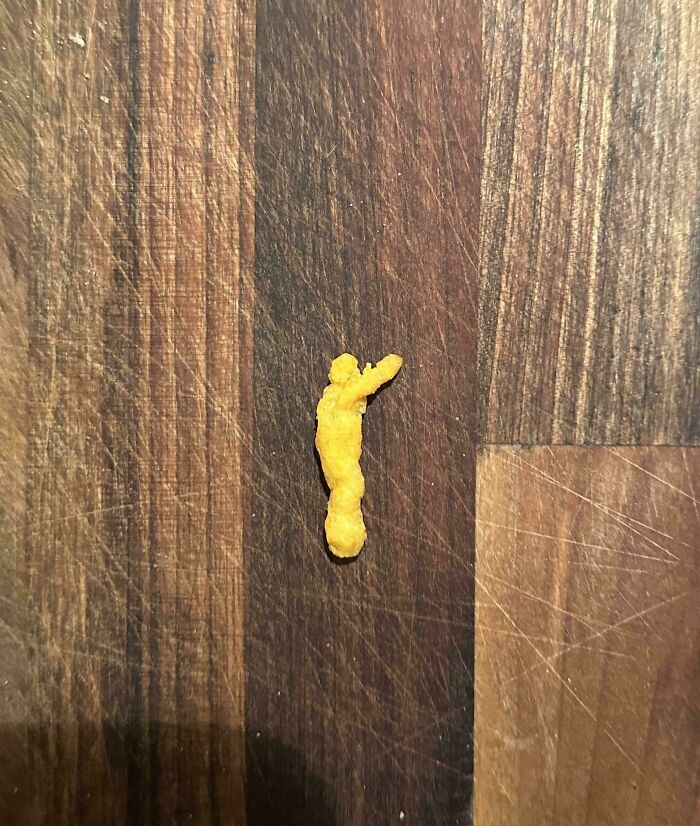 Unusual Cheeto shape resembling a person on a wooden surface, nothing particularly interesting about it.