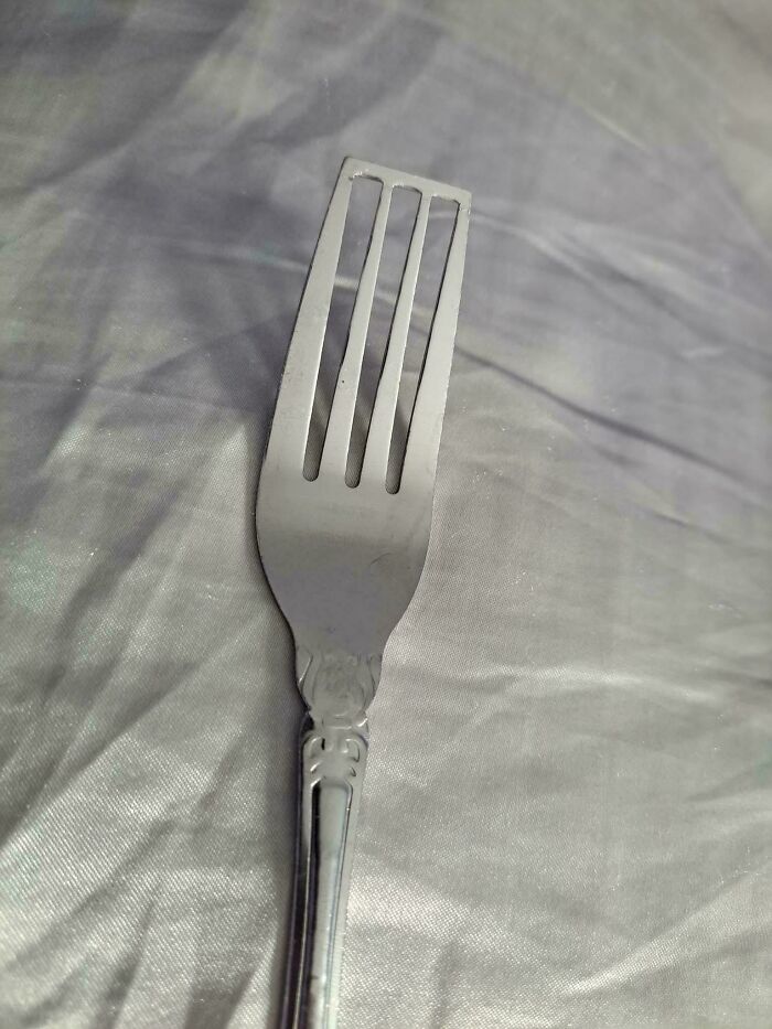 A metal fork lying on a plain, wrinkled gray surface, showcasing simple design features.