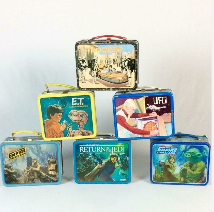 Vintage 1980s lunchboxes featuring Star Wars, E.T., and UFO designs stacked against a plain background.
