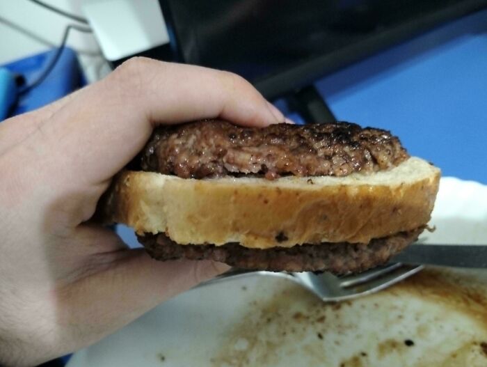 Person holding a simple burger with plain bread at a table.