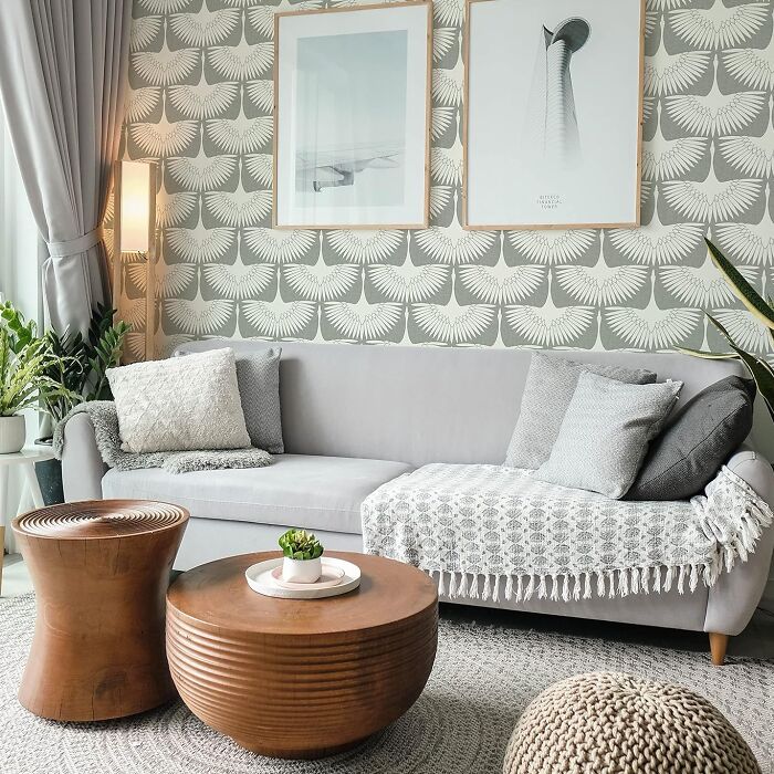 Cozy living room with DIY decor, patterned wallpaper, and a grey sofa with cushions and a knit throw.