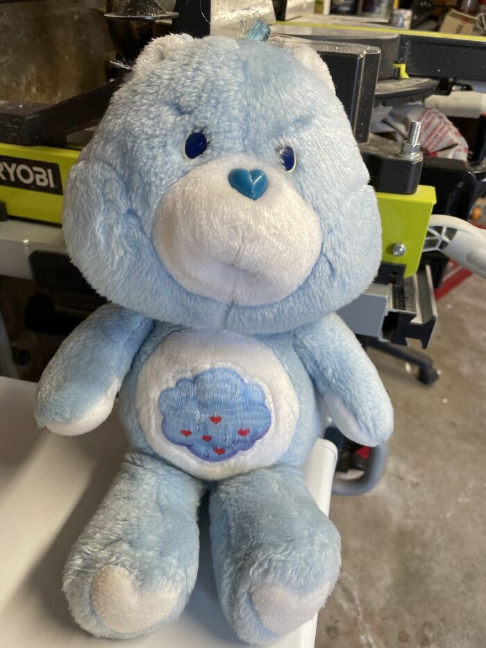 1980s blue teddy bear with a cloud emblem on its belly, sitting on a table in a workshop setting.