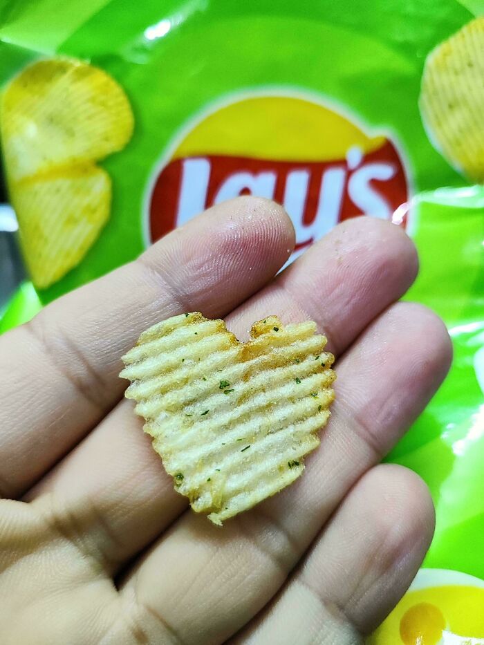 Heart-shaped potato chip held in hand with Lay's packaging in background.