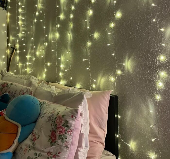 Fairy lights above a cozy bed with floral pillows and stuffed animals, perfect for a simple DIY home project.