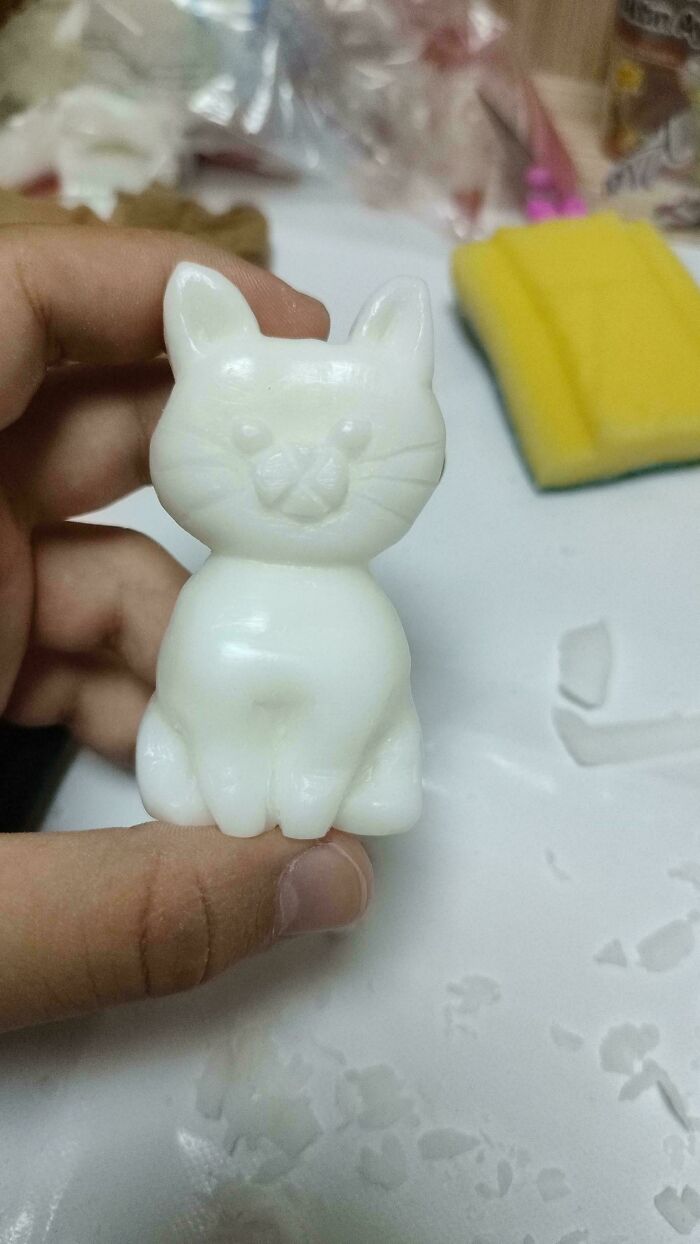Hand holding a small, white cat-shaped soap figurine.
