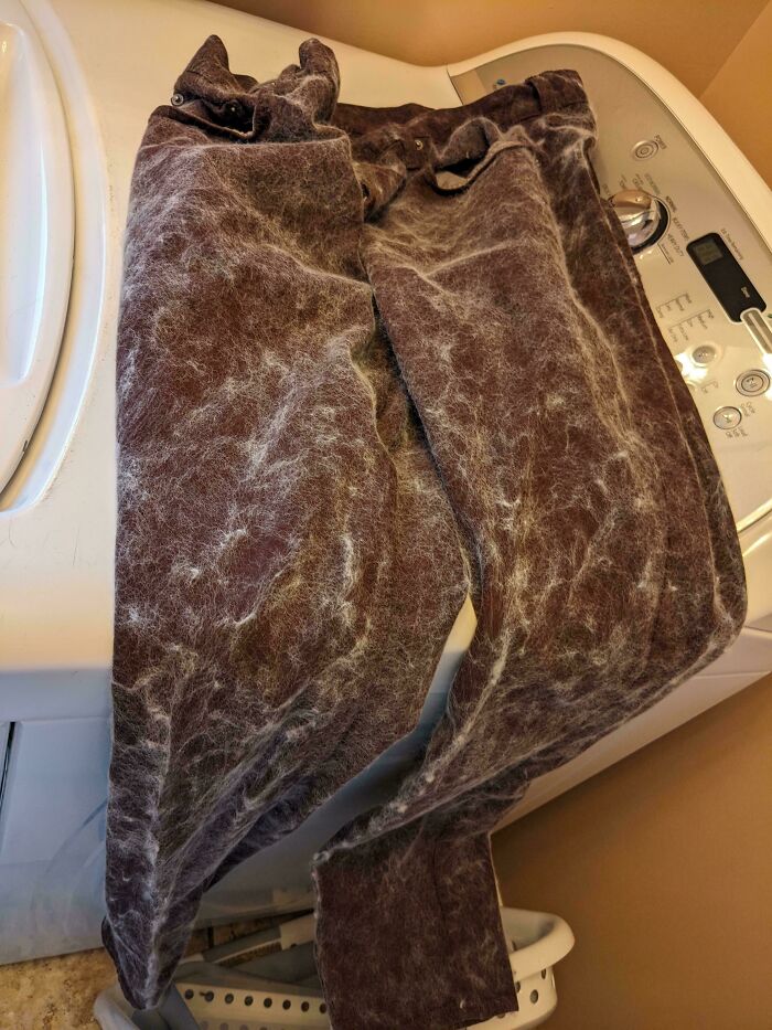 Pantalones oscuros llenos de pelusa sobre lavadora, mostrando un error en la lavandería.