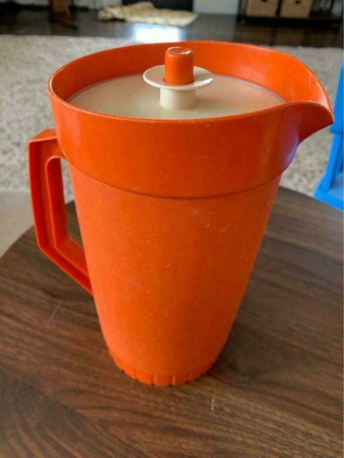 Orange 1980s vintage pitcher with lid, sitting on a wooden table.