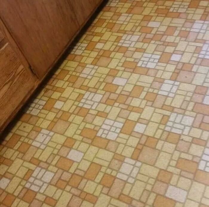 Retro 1980s kitchen floor with geometric orange and yellow tile pattern next to wooden cabinets.