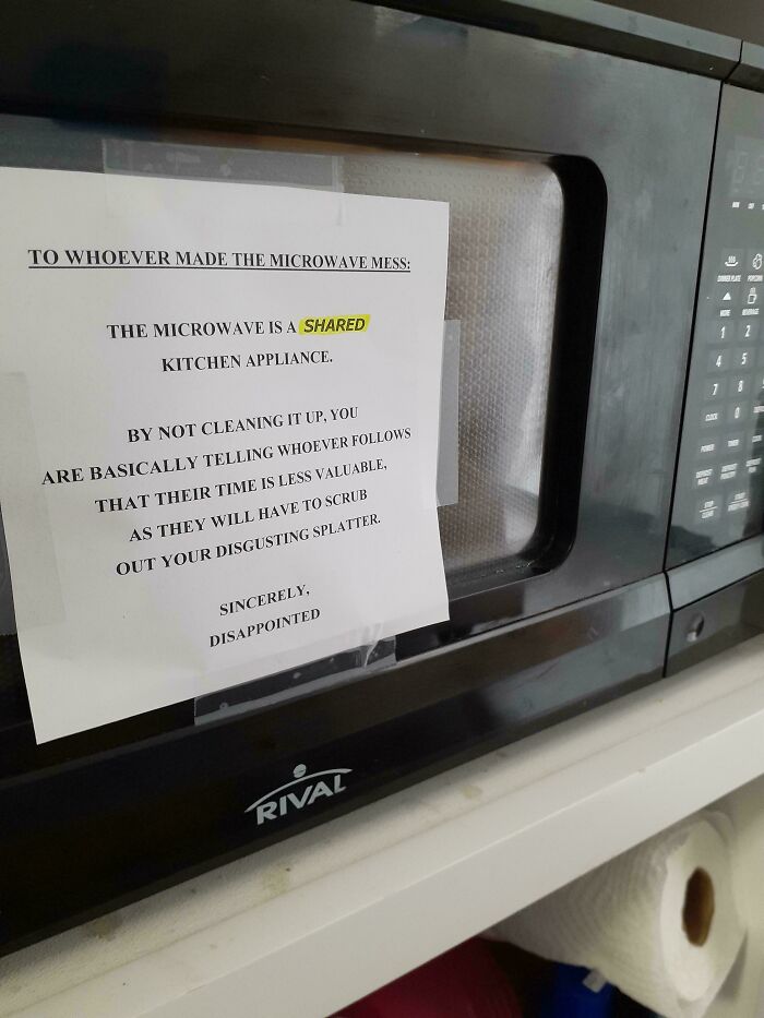 Passive-aggressive note on microwave about cleaning shared spaces, emphasizing considerate behavior and communal responsibility.