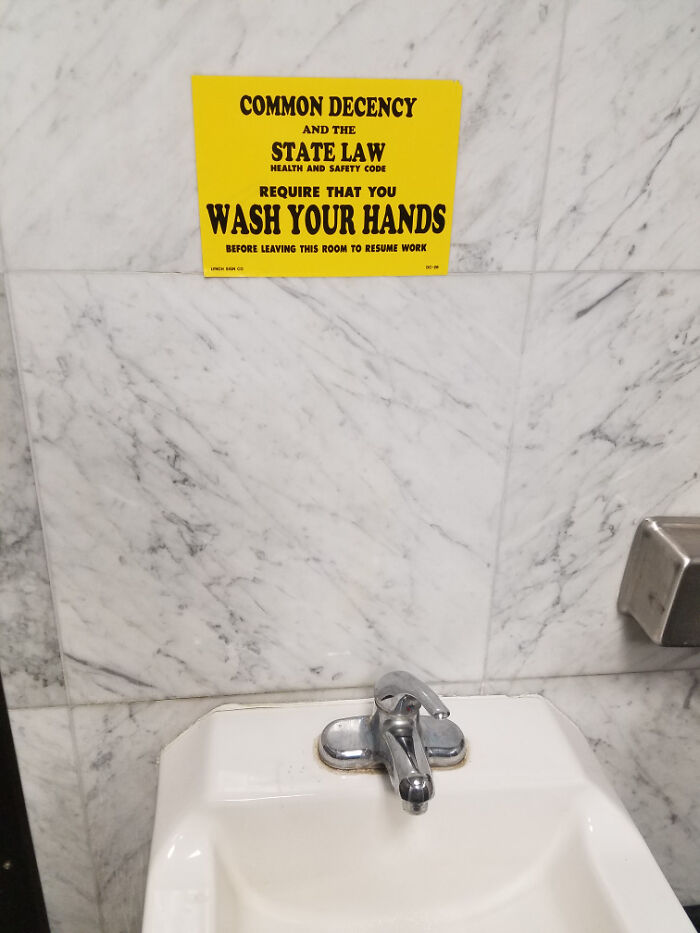 Sign on marble wall with passive-aggressive reminder to wash hands, citing state law and common decency.