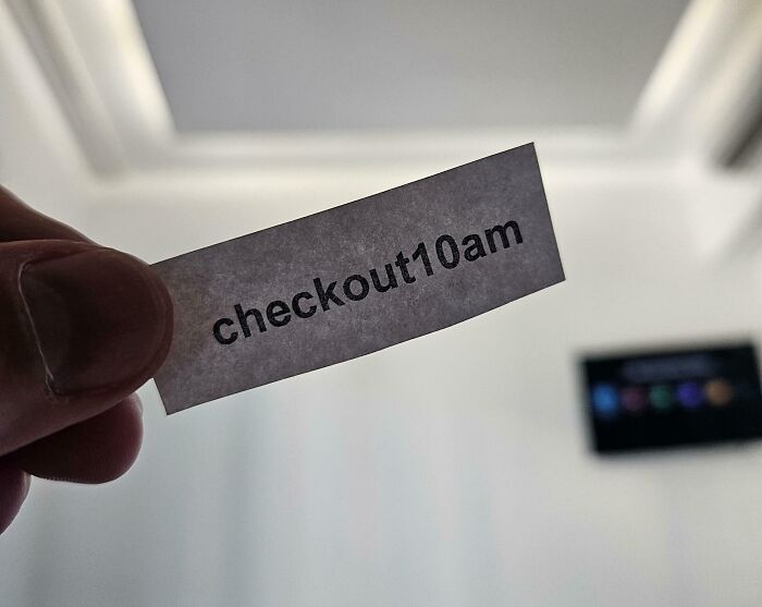 Passive-aggressive note reading "checkout 10am" held up against a blurred interior background.