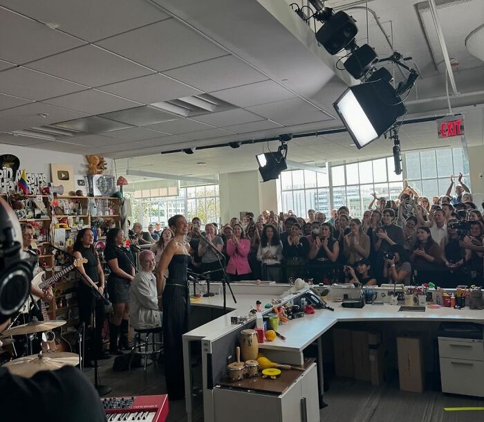 Live band performance in a crowded office space with an iconic setting, featuring musicians and an audience applauding.