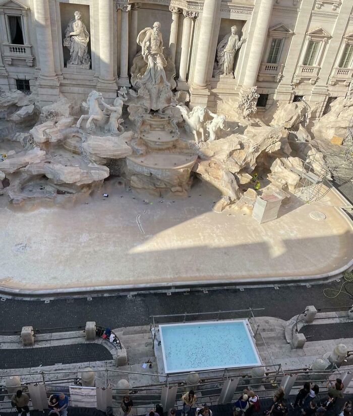 Empty Trevi Fountain in Rome, an iconic place under renovation, surrounded by scaffolding and tourists.