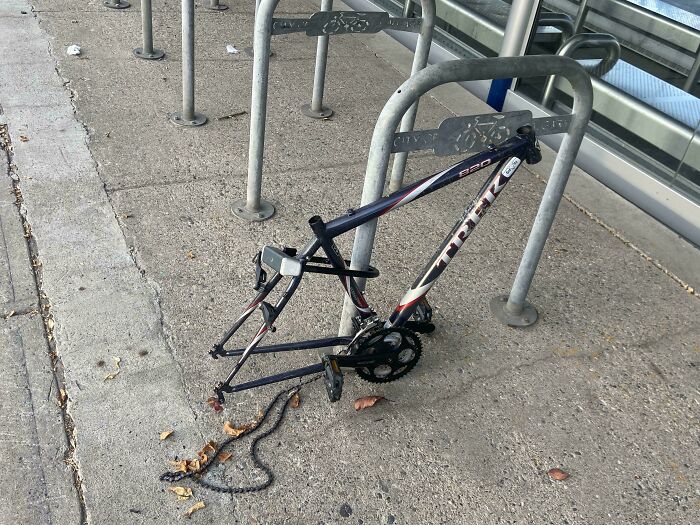 Broken bike frame locked to rack, missing wheels; a worst day at work moment.