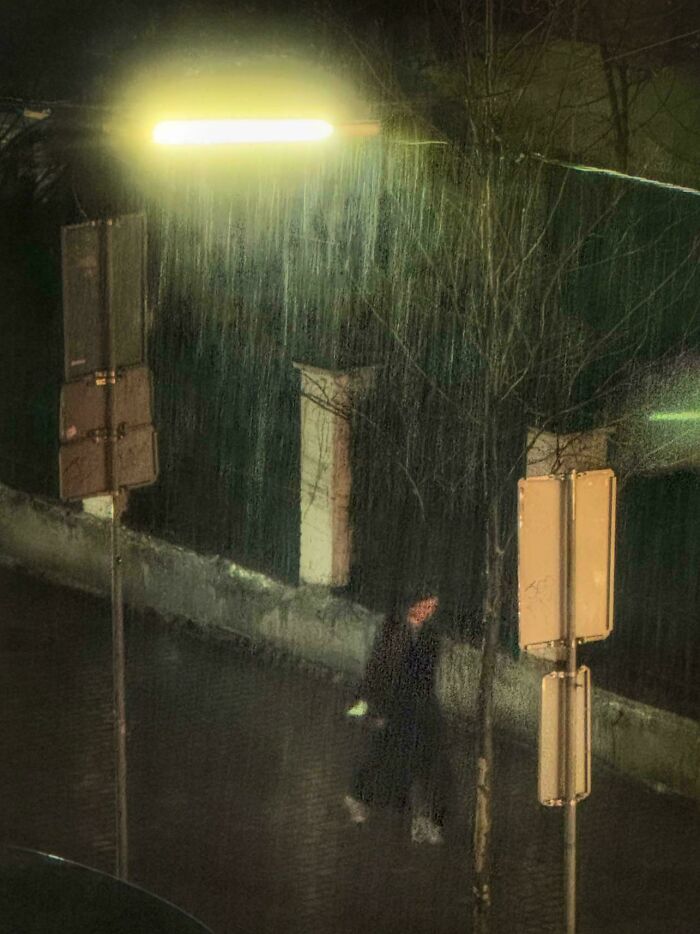 Person walking in the rain under a glowing streetlight, resembling a captured Renaissance masterpiece moment.
