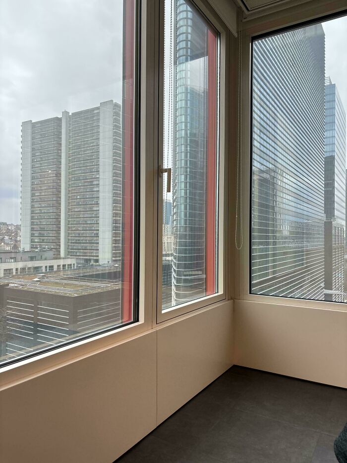View from inside an office corner overlooking tall buildings with windows demonstrating ignored safety protocol risks.