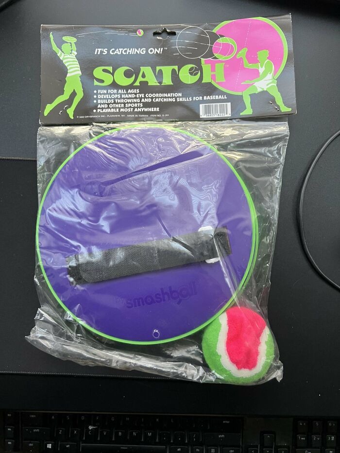 90s nostalgic toy Scatch catching game with purple paddle and colorful ball in original packaging on black surface.