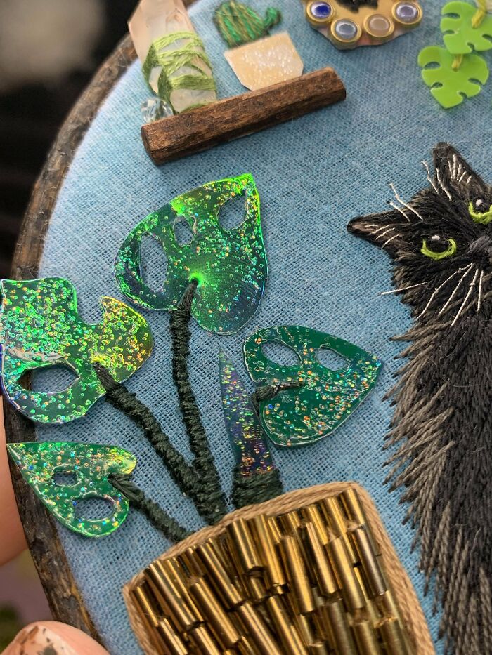 DIY project featuring a glittery plant with black cat embroidery on blue fabric.