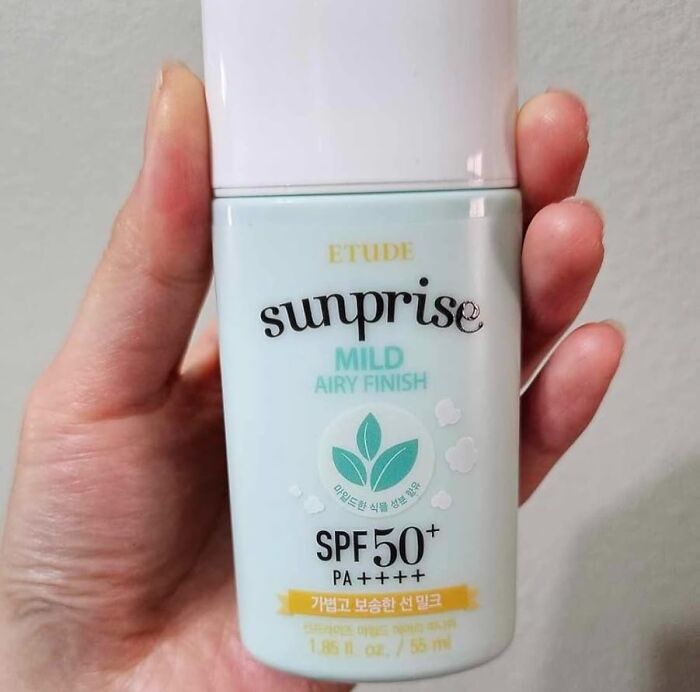 SPF 50 sunscreen bottle labeled "Sunprise Mild Airy Finish" held in a hand.