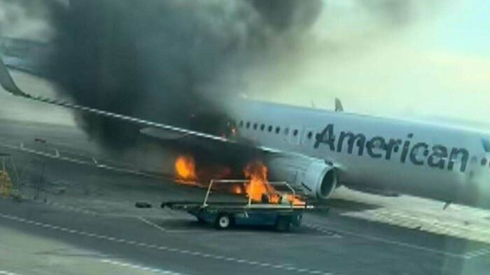 An American Airlines plane on fire, with thick black smoke billowing, a dramatic accident showing expensive damage.