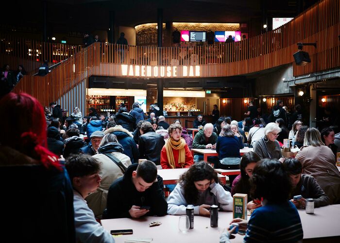 Crowded indoor bar scene with people seated at tables, capturing a moment resembling a Renaissance masterpiece.