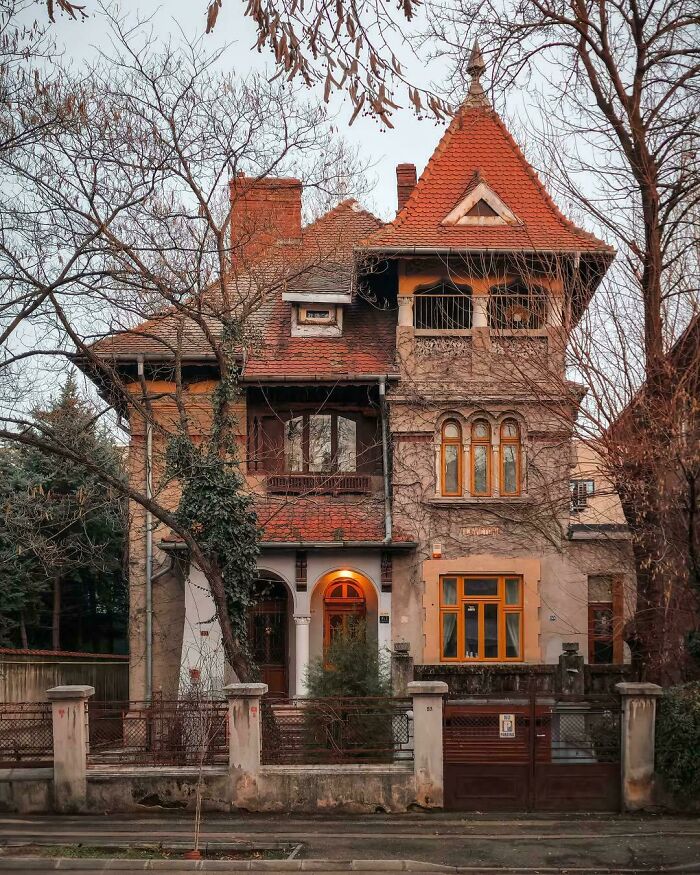 Historic house with detailed architectural feats and ornate roof design surrounded by leafless trees in autumn.