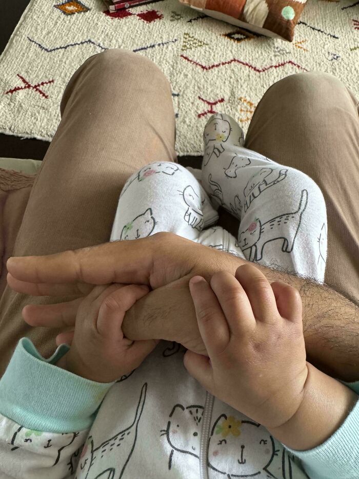 Baby holding dad's hand while sitting on his lap, capturing wholesome dads parenting moments with toddler in cozy setting.