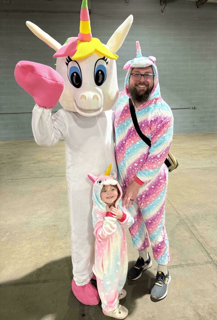 Dad and child in matching unicorn pajamas with person in unicorn costume sharing wholesome parenting moment