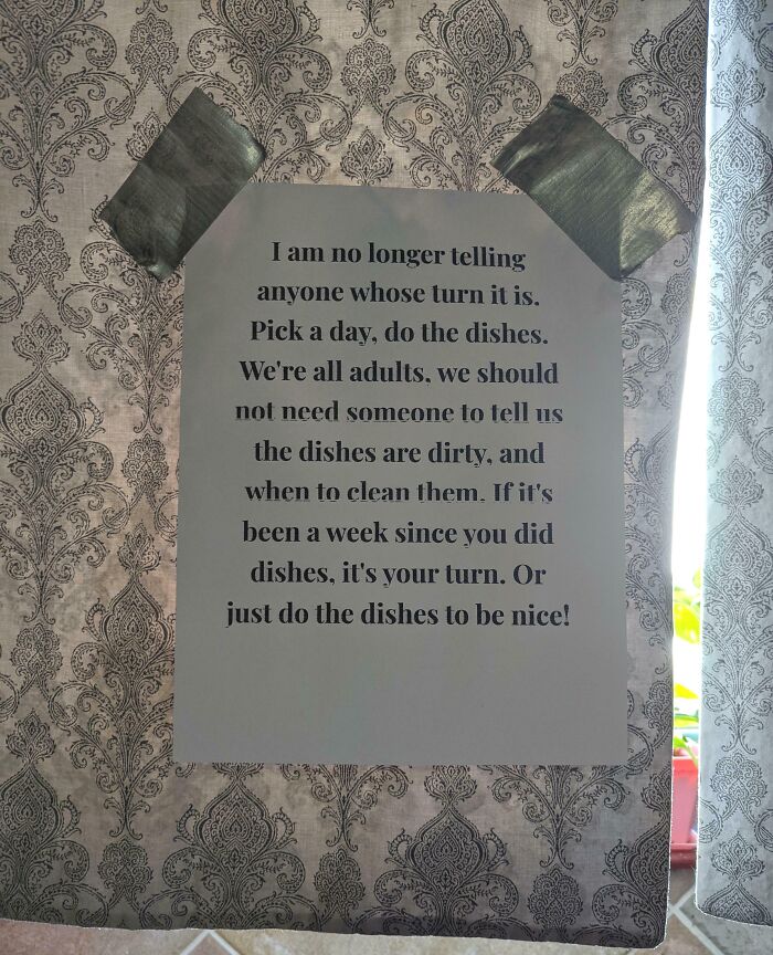 Passive-aggressive note about doing the dishes, taped to a patterned wall.
