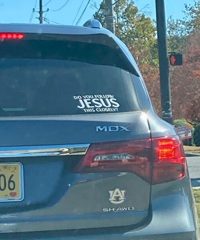 A car with a passive-aggressive bumper sticker asking, "Do you follow Jesus this closely?" at a traffic light.