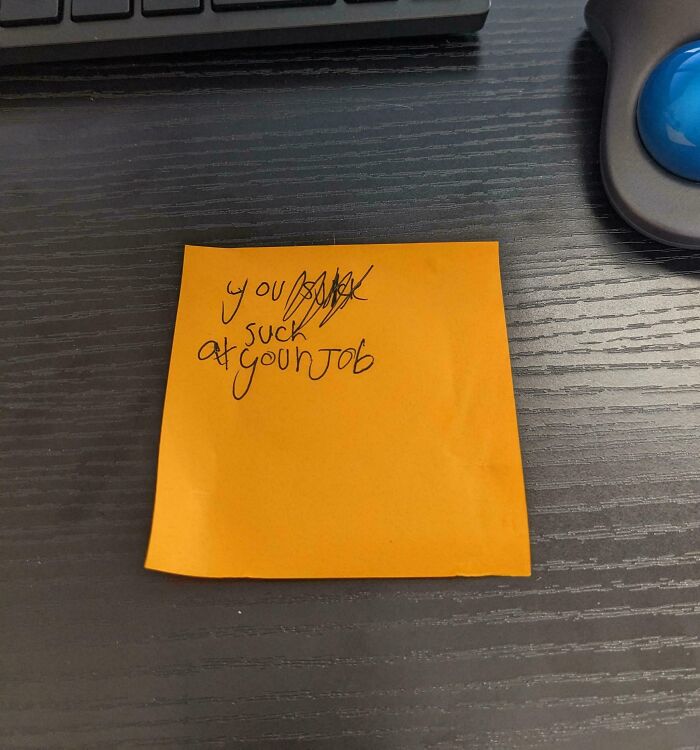 A funny passive-aggressive note on a desk says, "You suck at your job," with edits.