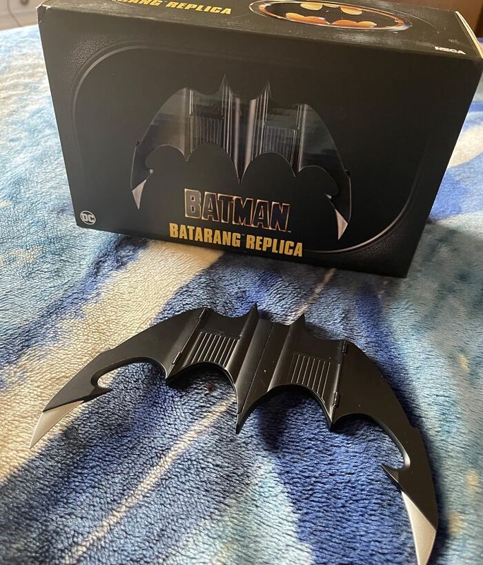 Batman Batarang replica movie prop displayed with its packaging on a blue surface.