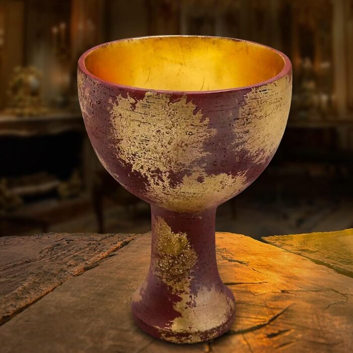Aged golden chalice, an awesome movie prop, resting on a rustic wooden table in a dimly lit room.