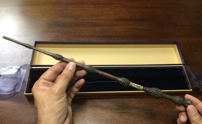 Hands holding a replica movie prop wand in front of an open box.