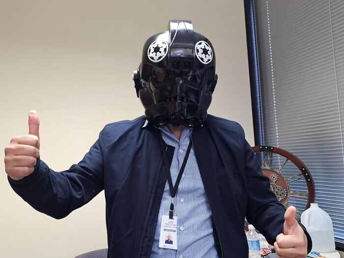 Person wearing black movie prop helmet, giving thumbs up.