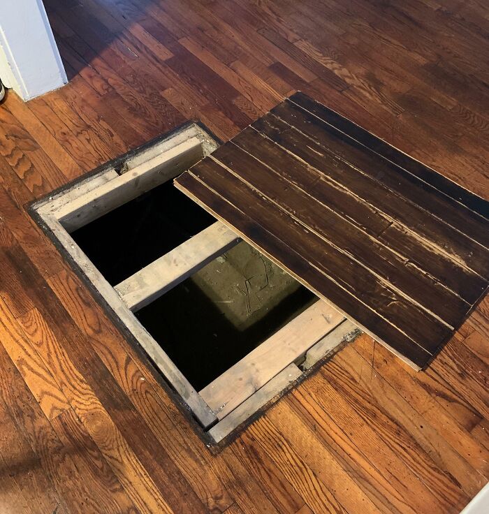 Hidden trapdoor discovered in old house floor, revealing a secret compartment underneath.