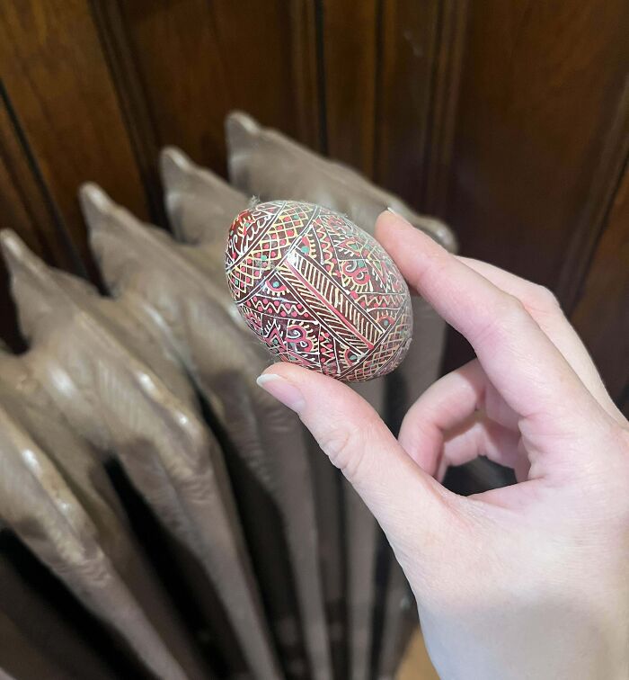 Hand holding a decorative artifact egg with intricate patterns in front of a wooden background.