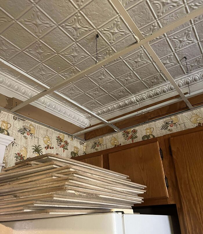 Vintage ceiling tiles in an old house kitchen with floral wallpaper and wooden cabinets, showcasing artifacts from the past.