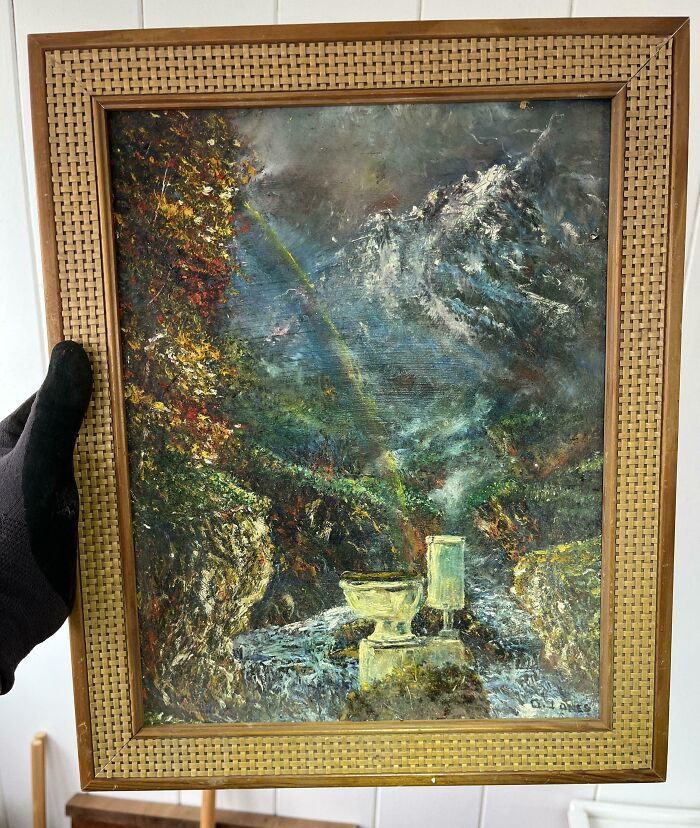 Vintage painting depicting a mountain scene with a rainbow, discovered in an old house, framed in a wicker-bordered frame.