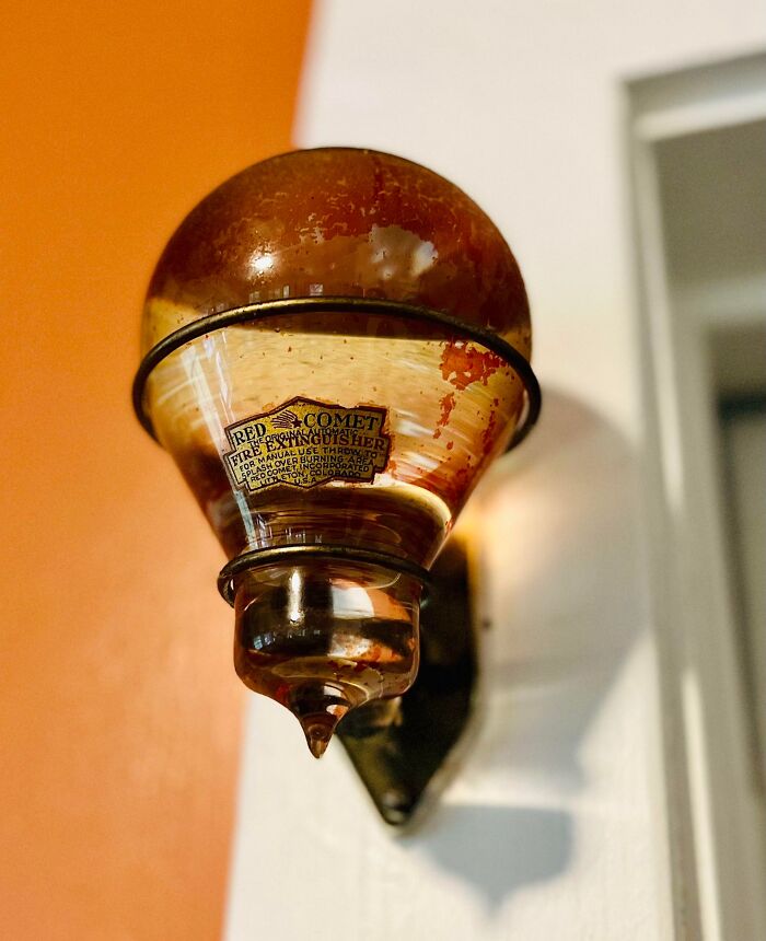 Vintage Red Comet fire extinguisher with red liquid, mounted on a wall; an intriguing artifact from the past.