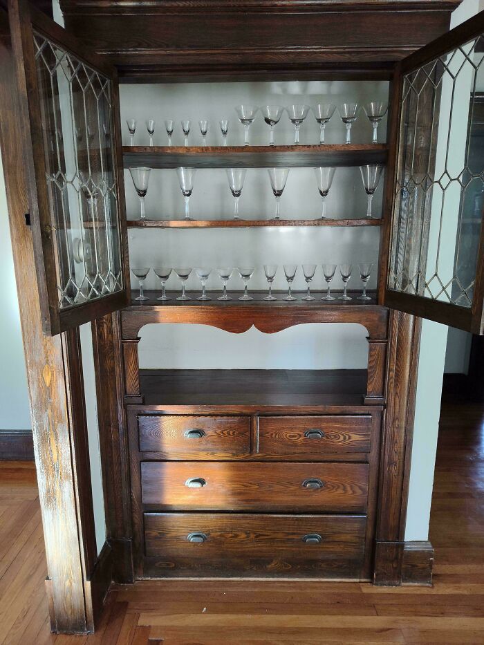 Vintage wooden cabinet displaying glassware, found in an old house, highlighting artifacts from the past.