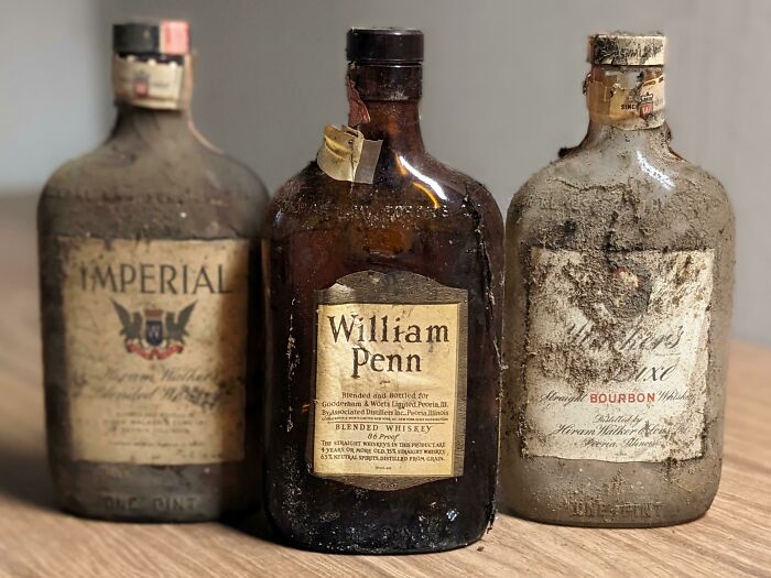 Three vintage whiskey bottles found in an old house, dusty and labeled Imperial, William Penn, and Bourbon.