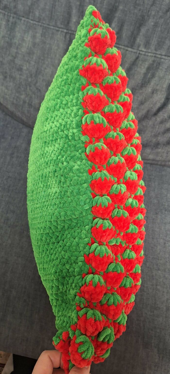 Green and red crochet pillow with textured strawberry pattern, crafted by crochet enthusiasts with intricate details.