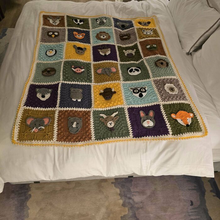 Crochet blanket featuring colorful animal faces crafted by crochet enthusiasts, displayed neatly on a bed.