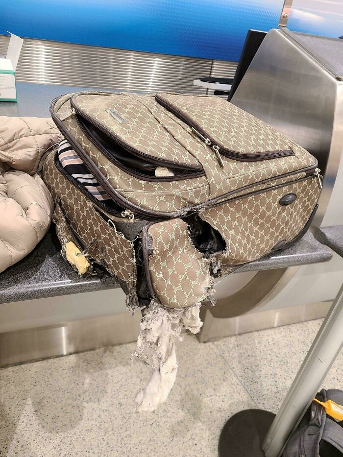 Damaged suitcase with torn fabric at airport check-in counter, depicting an epic airline baggage fail.