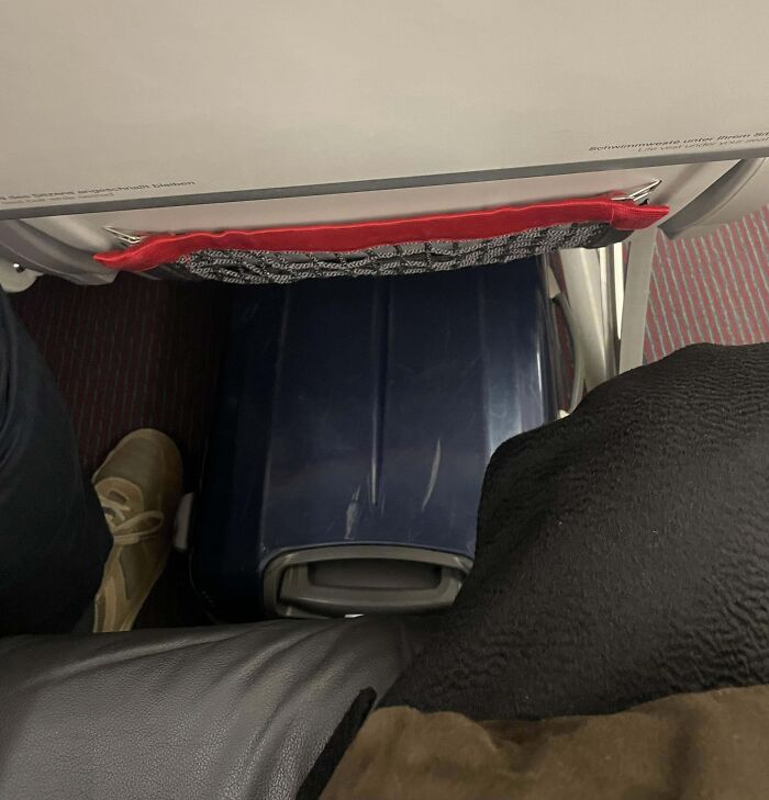 Airline baggage packed tightly under airplane seat, leaving minimal legroom.