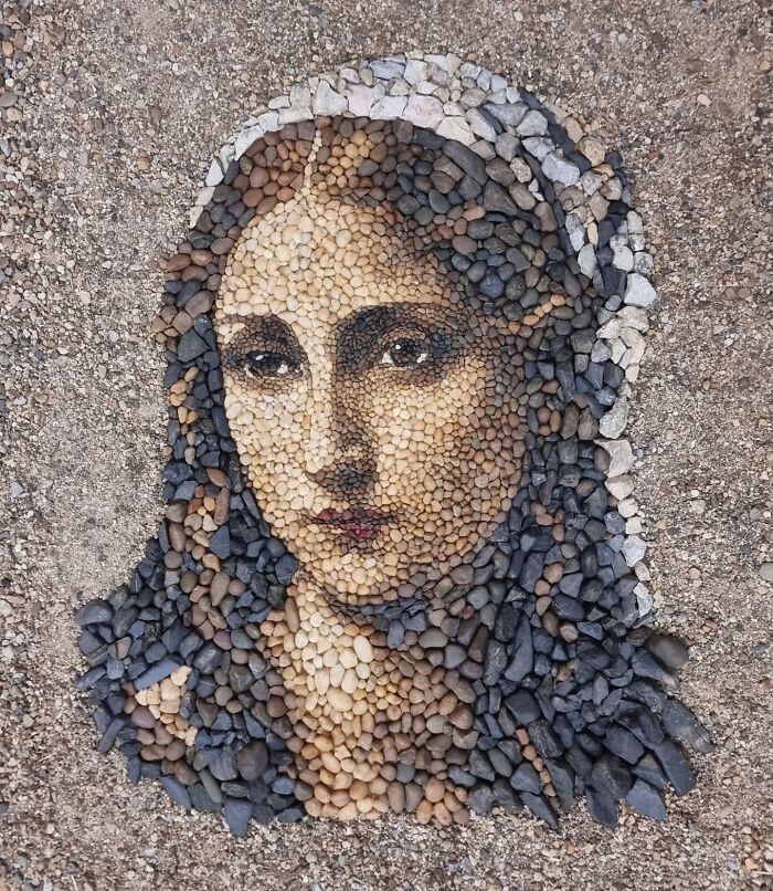 Stone and pebble mosaic artwork by a British artist, depicting a detailed portrait on a sandy surface.